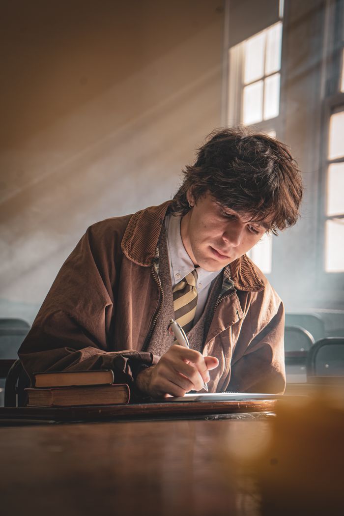 Young man writing in a sunlit classroom, focused on work.