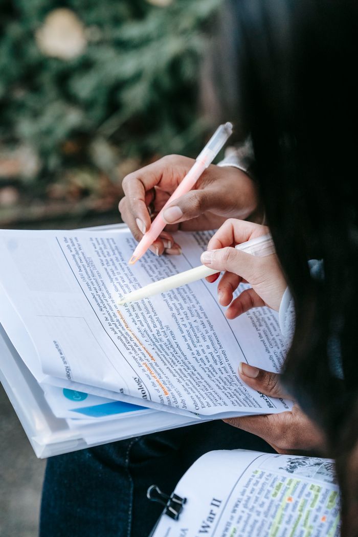 Crop anonymous diverse female students reading new learning material together and highlighting main information while sitting in park