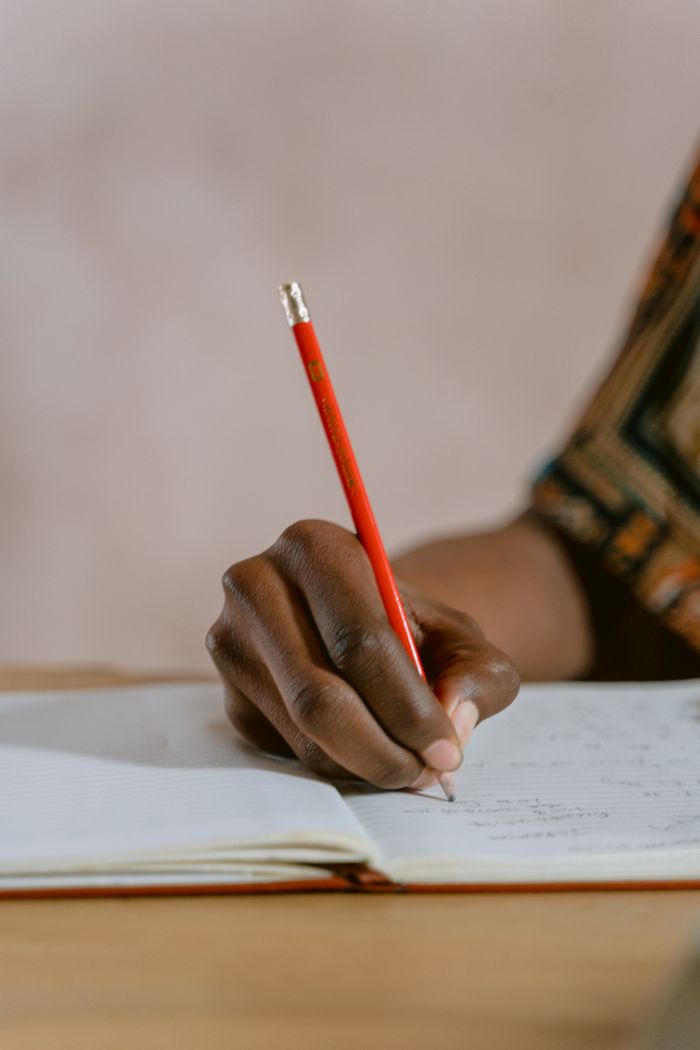 services-01 A person writing in a notebook with a red pencil, focusing on the hand's detail.